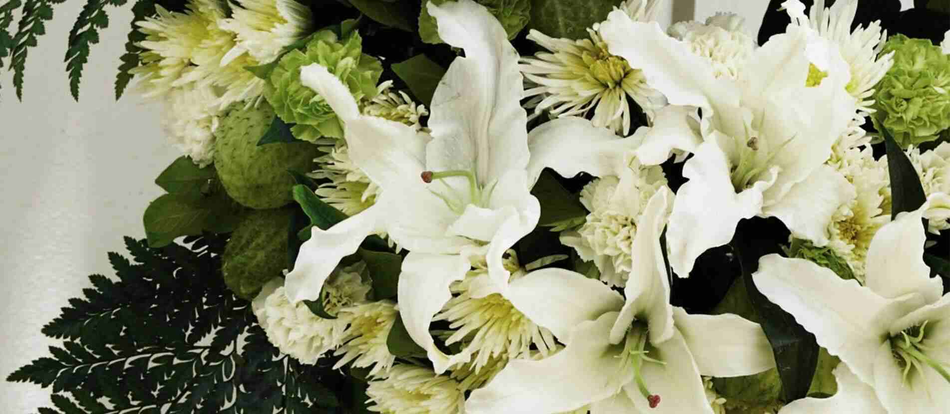 ดอกลิลลี่สีขาวล้อมด้วยดอกไม้หลายชนิดสำหรับจัดลงในพวงหรีดไว้อาลัย